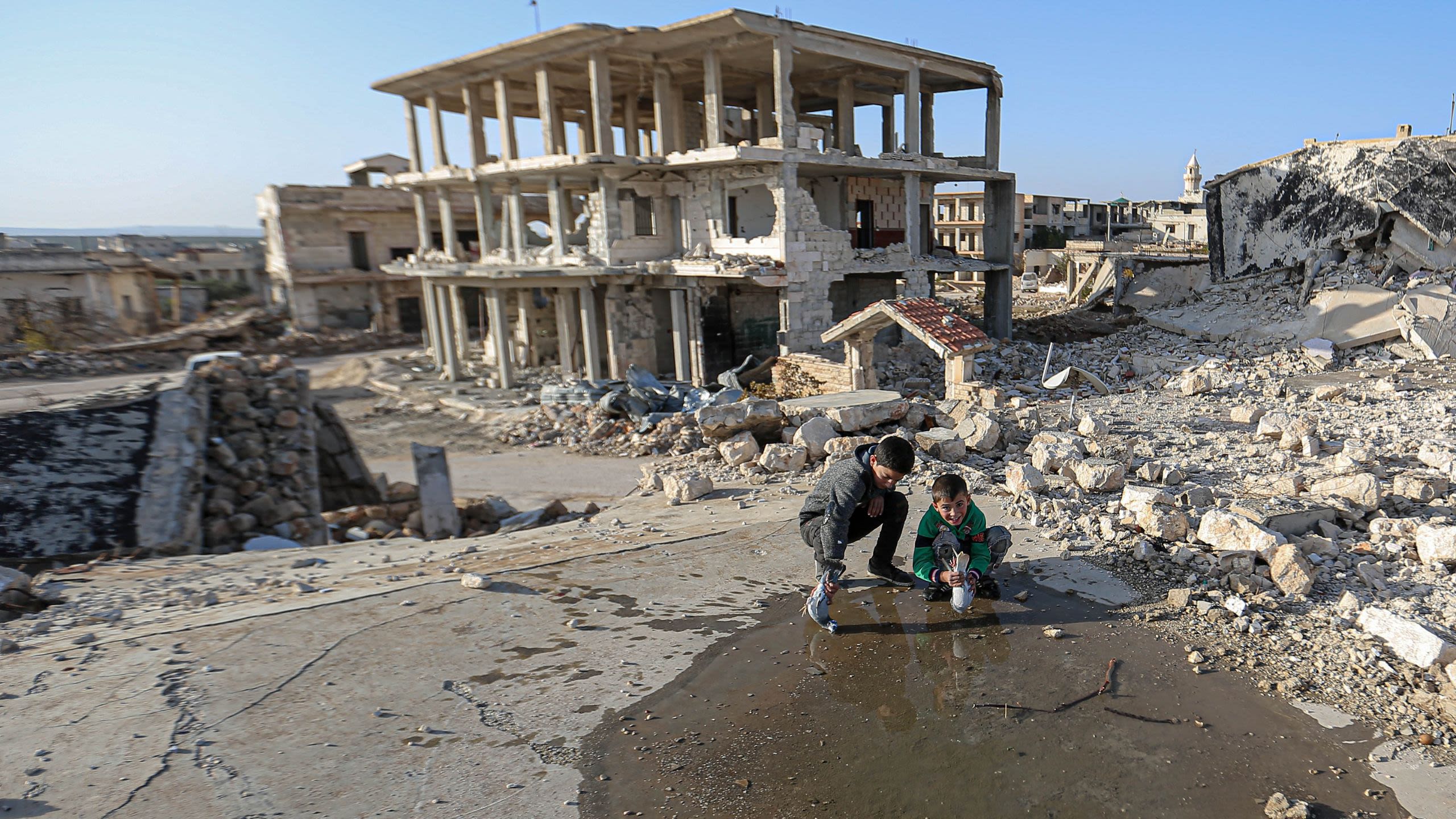 two boys trying to give birds a drink from a puddle in a bombed out area