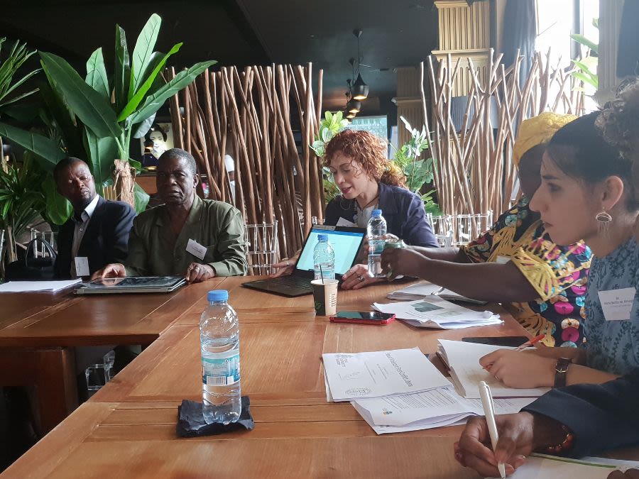 Ismene Gizelis showing her laptop screen whilst sitting at table with group of people in Africa.