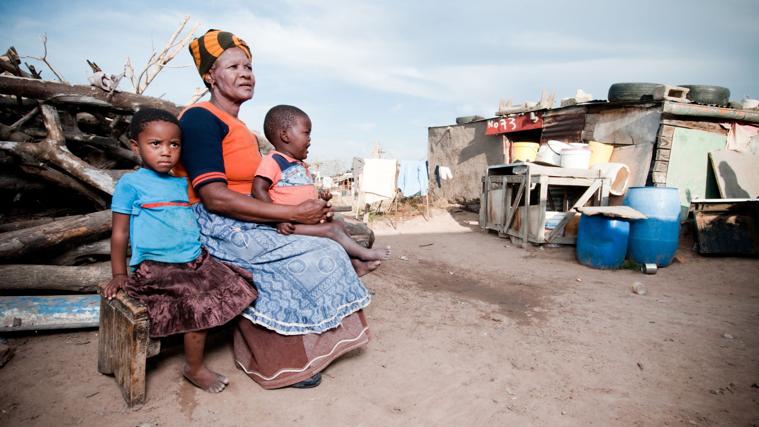 Woman in Africa sitting on bench beside a young girl and holding a toddler