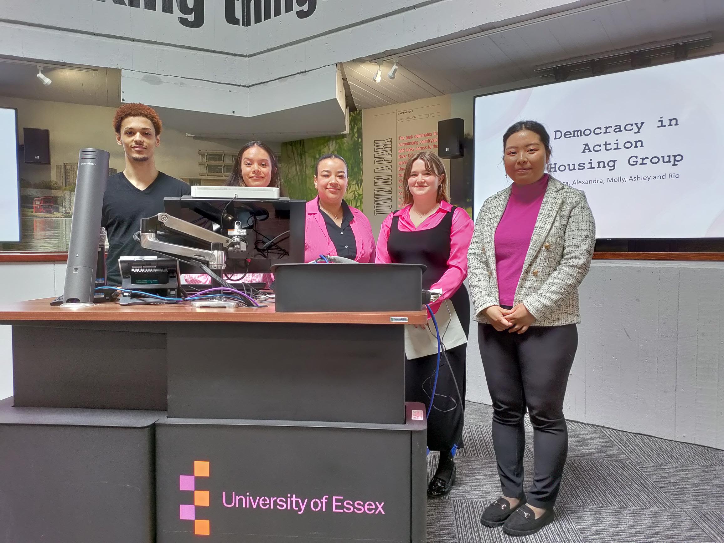 Presentation with 3 individuals standing behind a computer and presentation screen