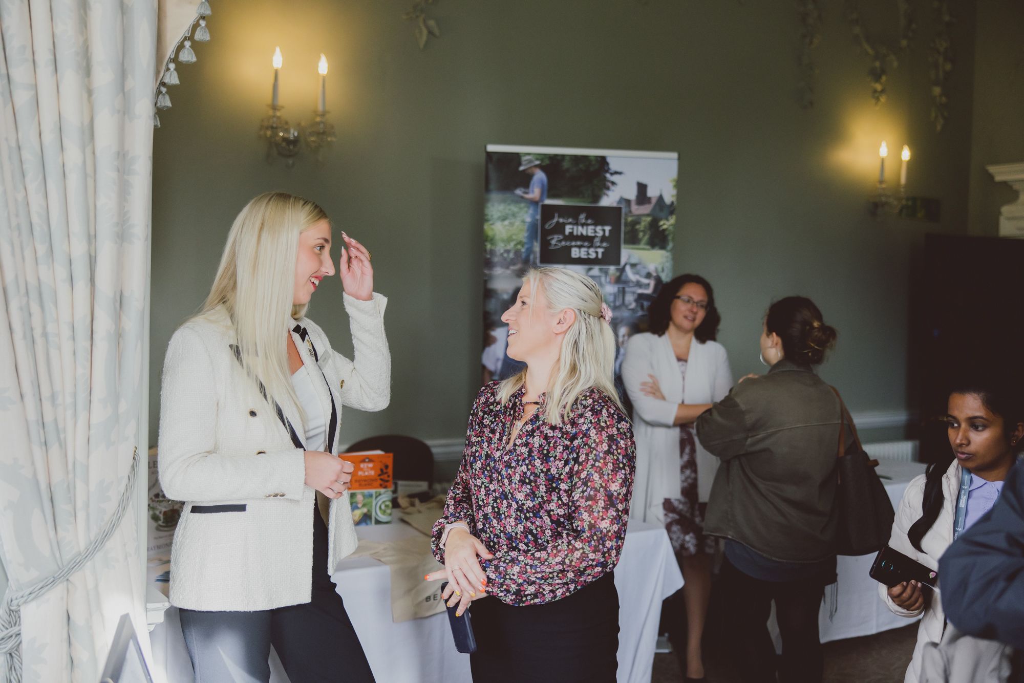 Two women, smiling and looking relaxed, chatting at a conference in a plush hotel