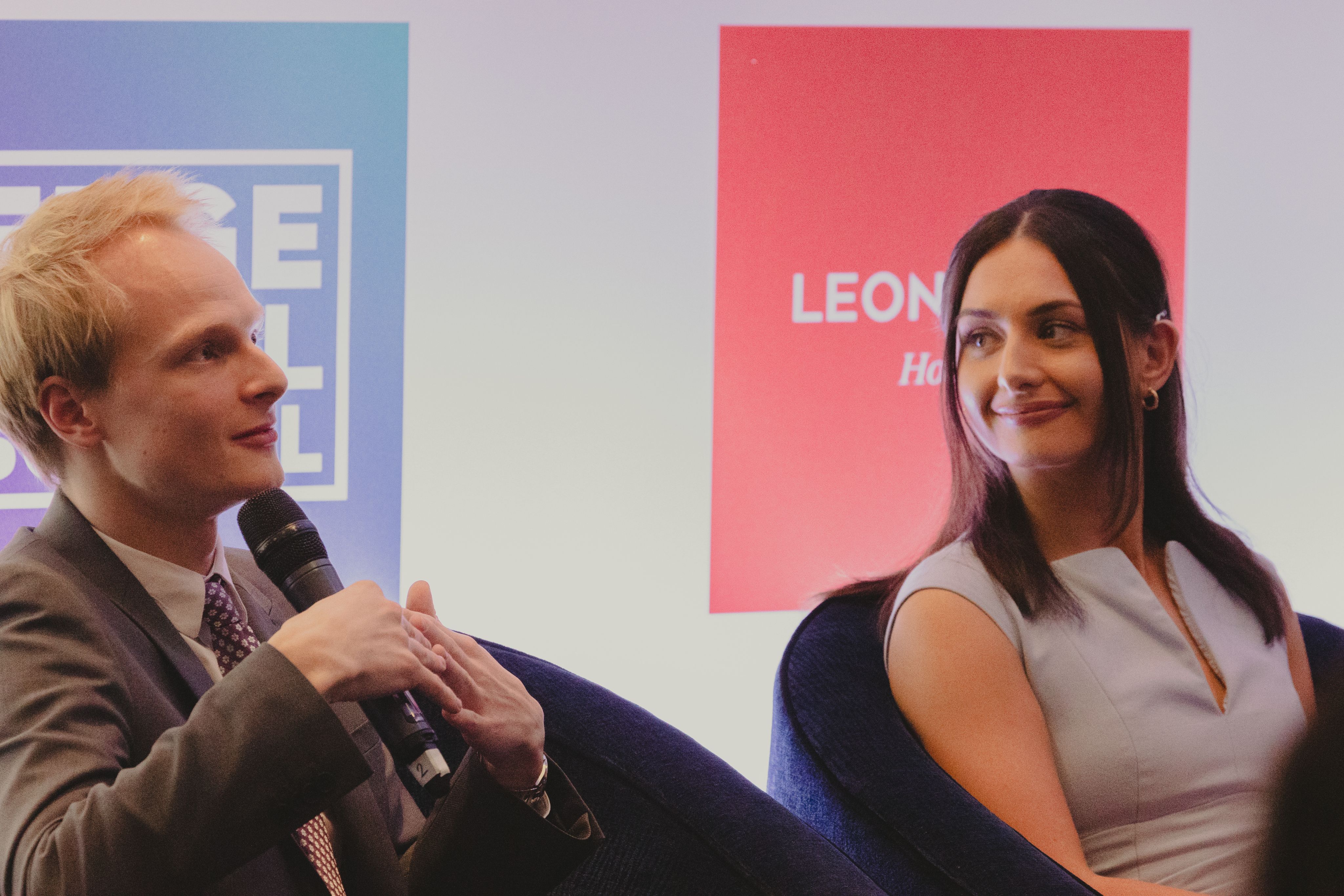 Two young professionals, one holding a microphone, speak on a panel of experts