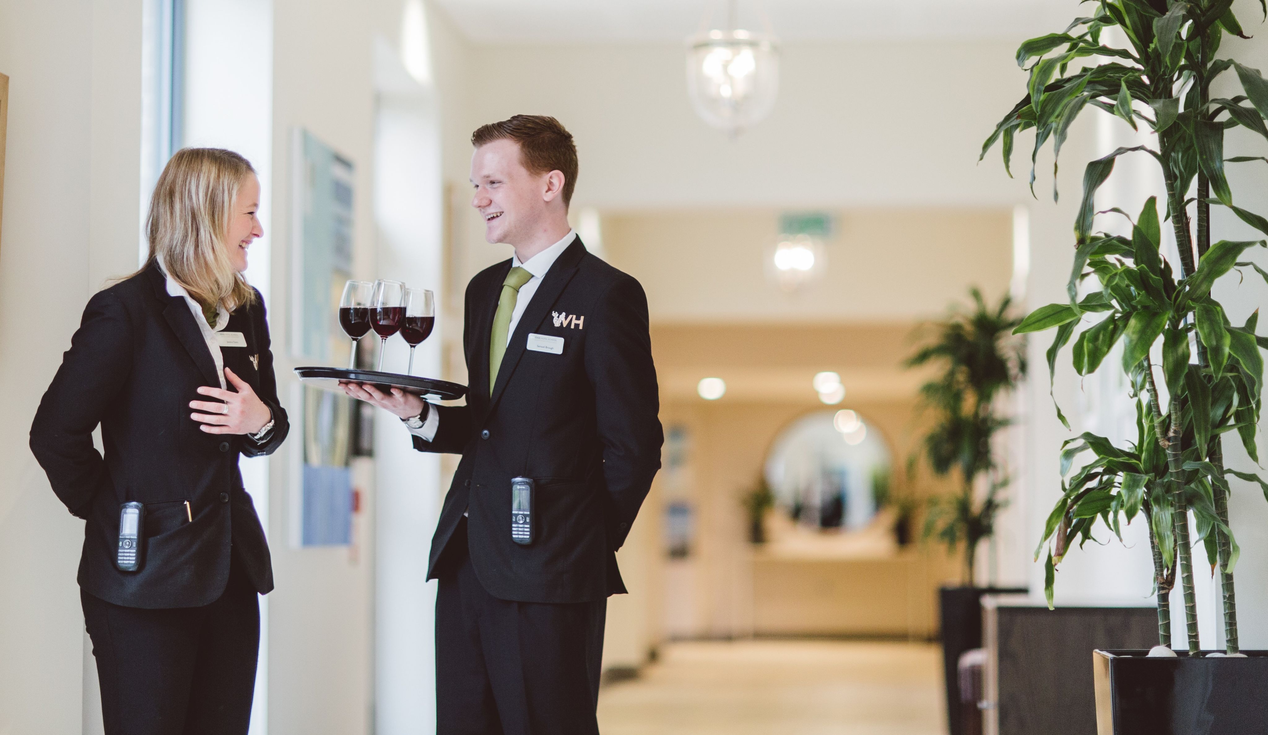 Two young hospitality professionals laughing as one holds a tray of wind glasses