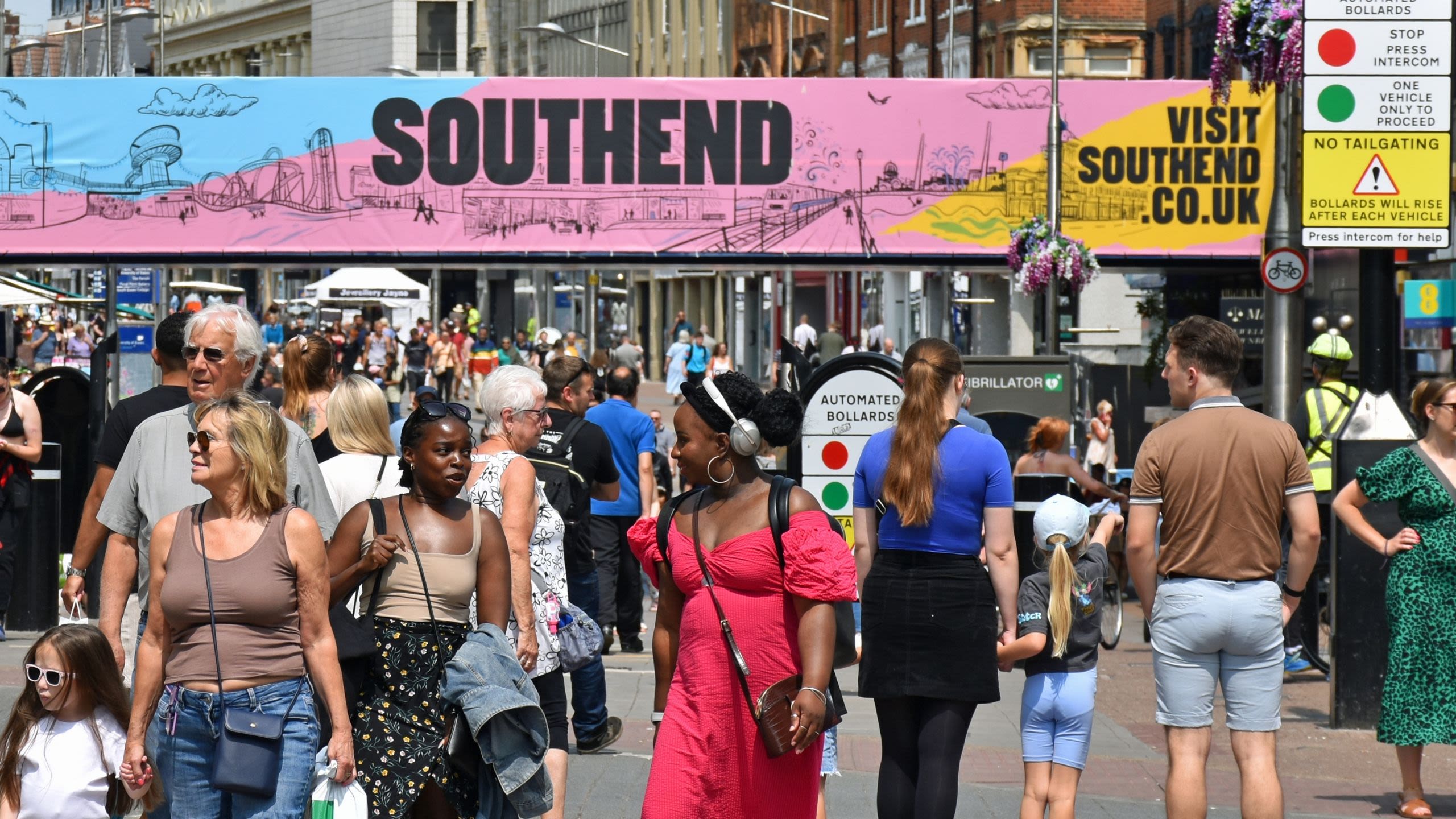 People walk along a sunny, crowded high street with a banner reading 'Southend' in the background