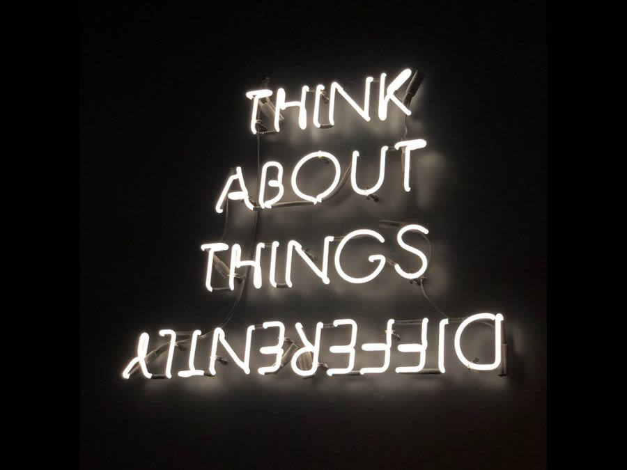 A neon sign reading 'THINK ABOUT THINGS DIFFERENTLY'. The word 'DIFFERENTLY' is written backwards.