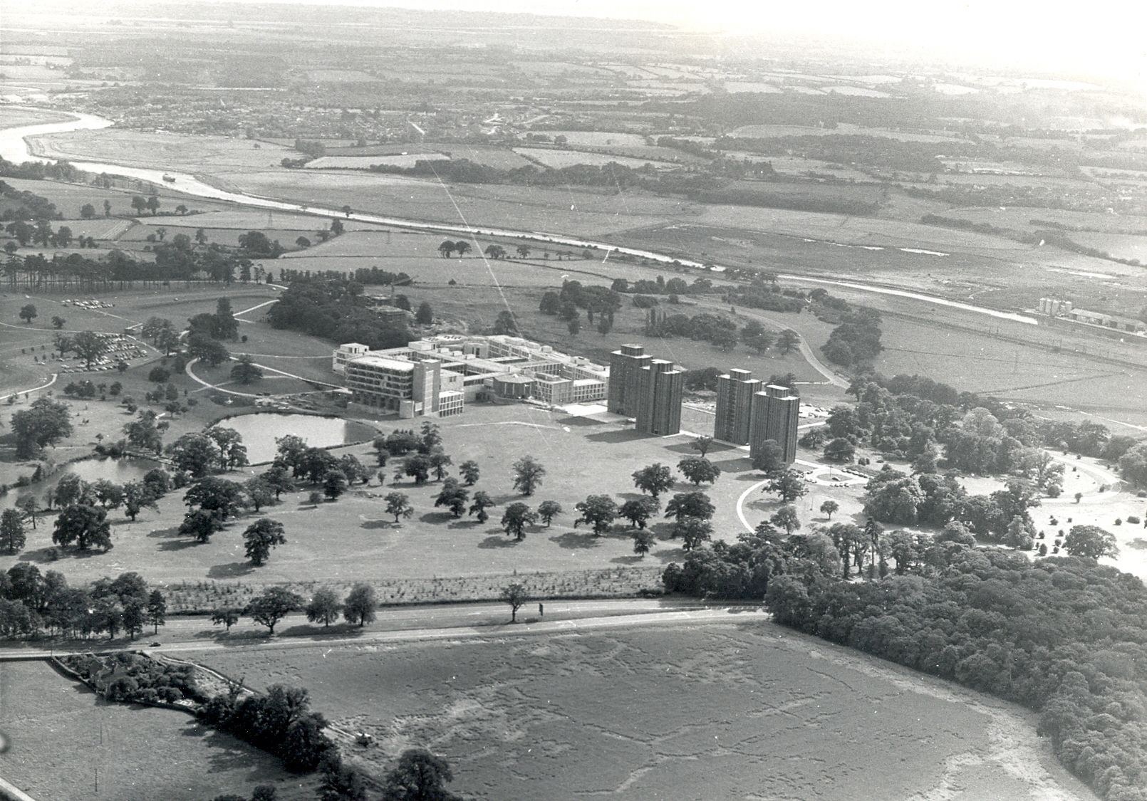 A black and white aerial photo of the University after construction nestled amidst the trees and meadows of Wivenhoe Park.