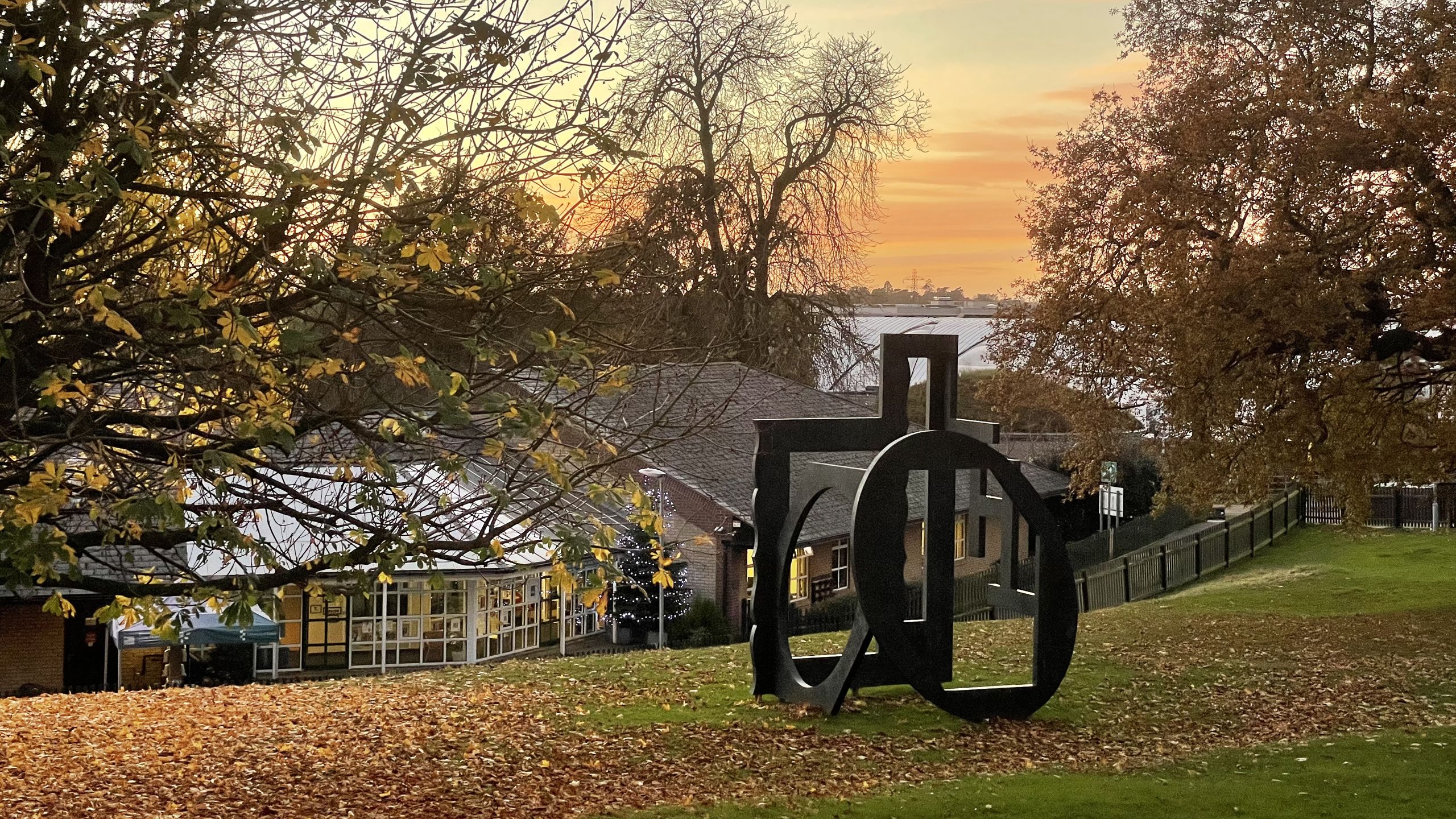 Views of the Interior, a metal sculpture of rectangular and oval windows, sits among autumn leaves as the sun sets over Wivenhoe Park.