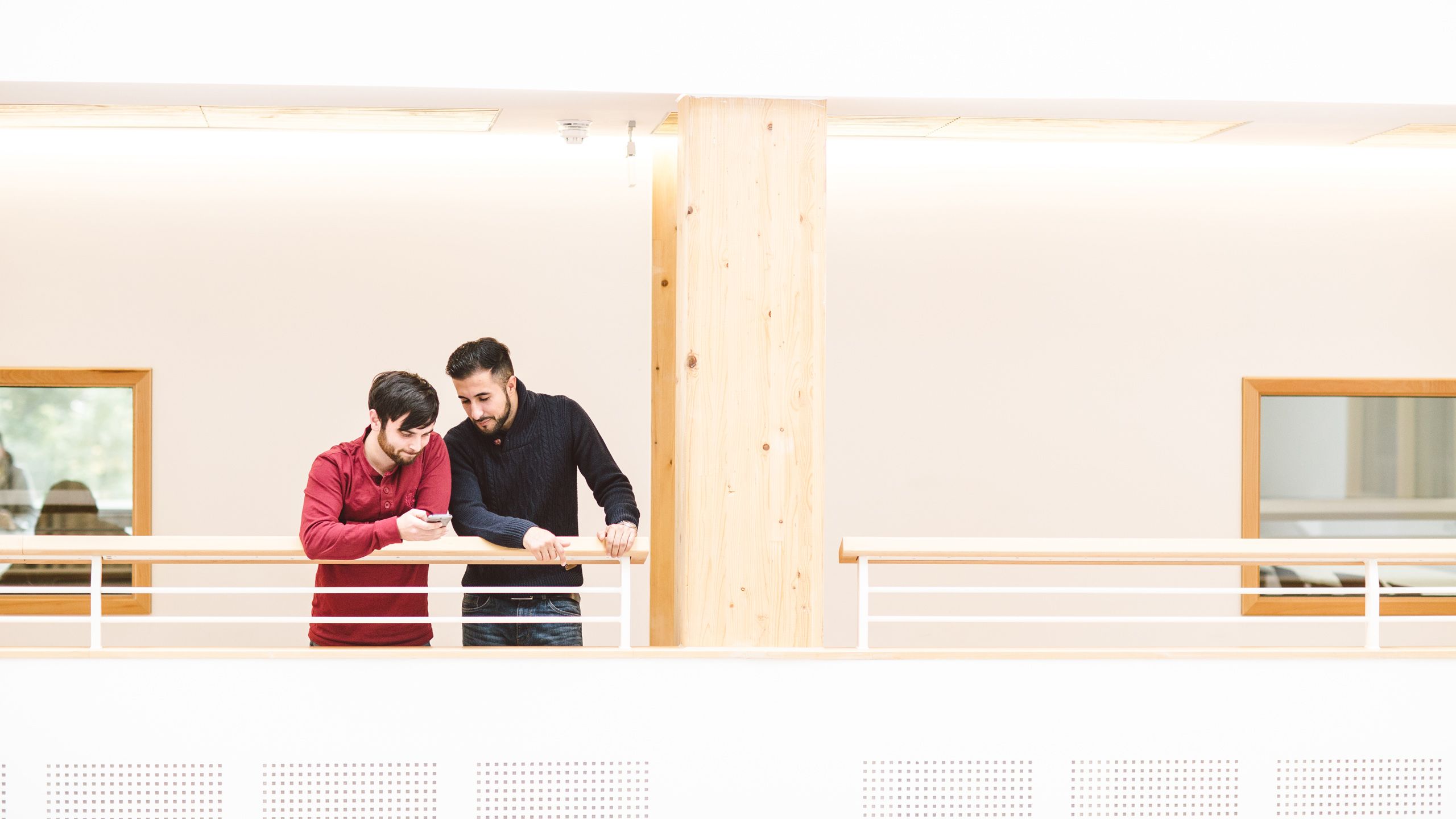 Two people stand on a light, airy balcony inside Essex Business School and look at a phone.