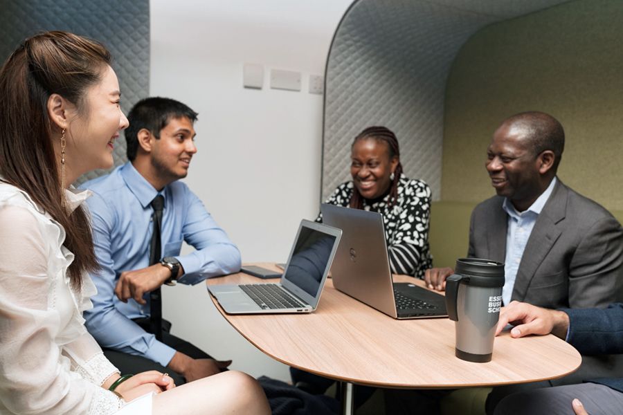Four academics smile during a discussion over laptops in a booth.