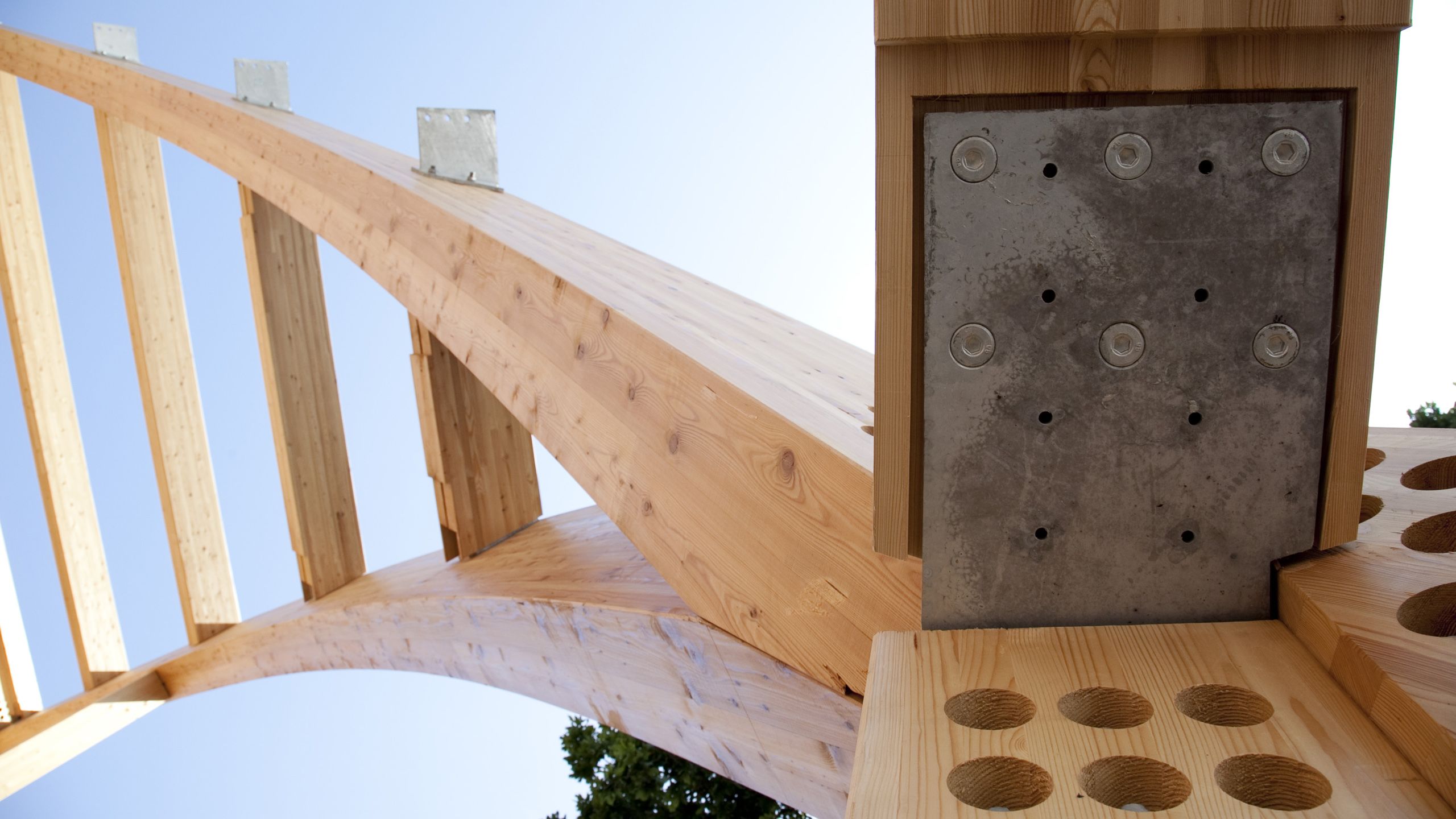 Timber arches reach skyward, fastened by a large array of bolts and metal plates.
