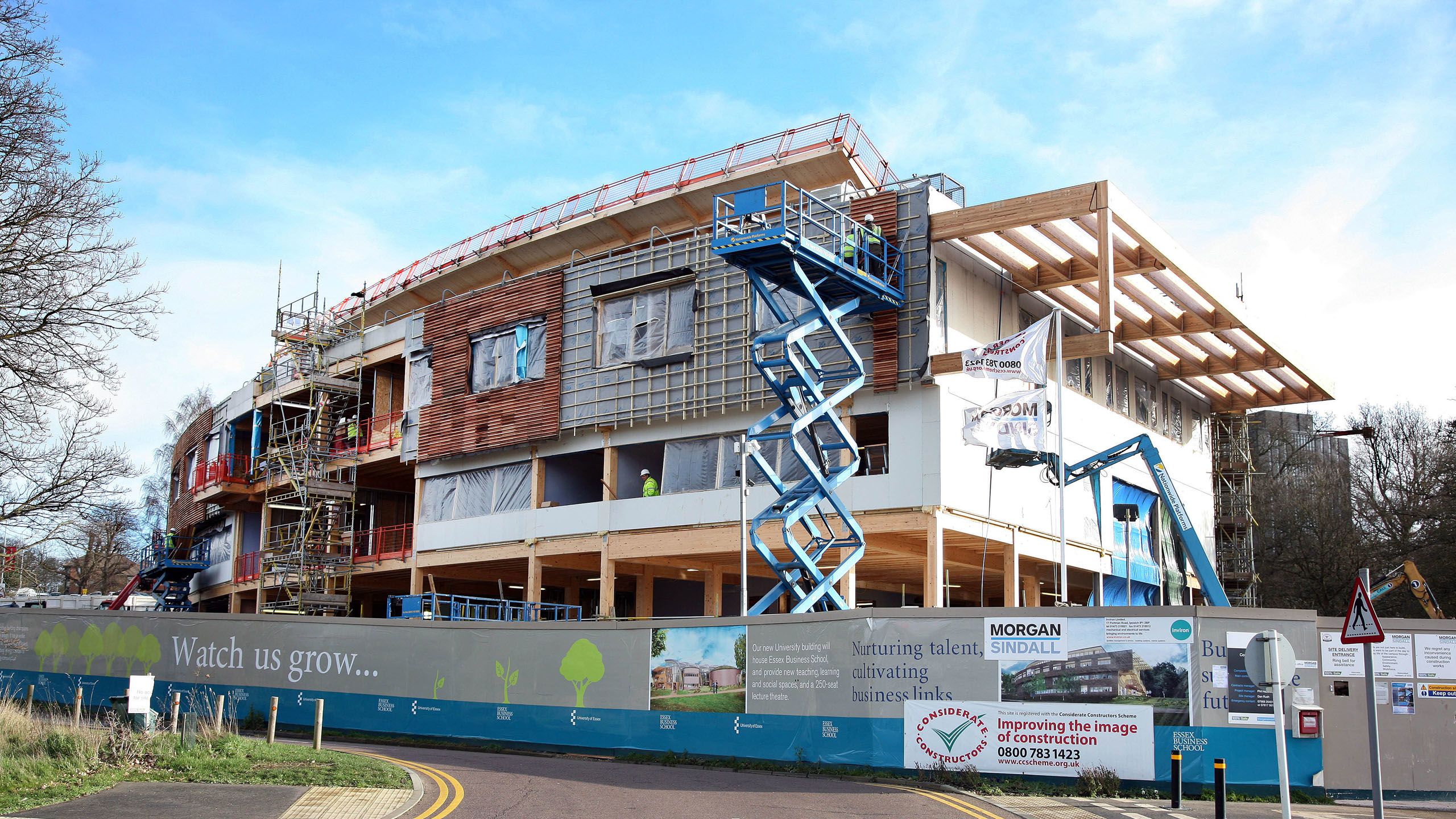 Workers use cherry pickers to apply wooden panels to EBS' exterior.