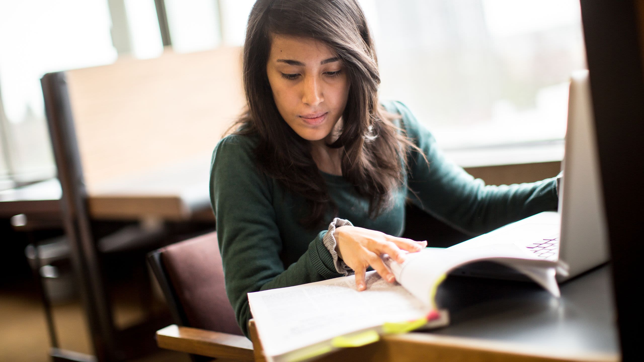 Student reading a book in front of a laptop