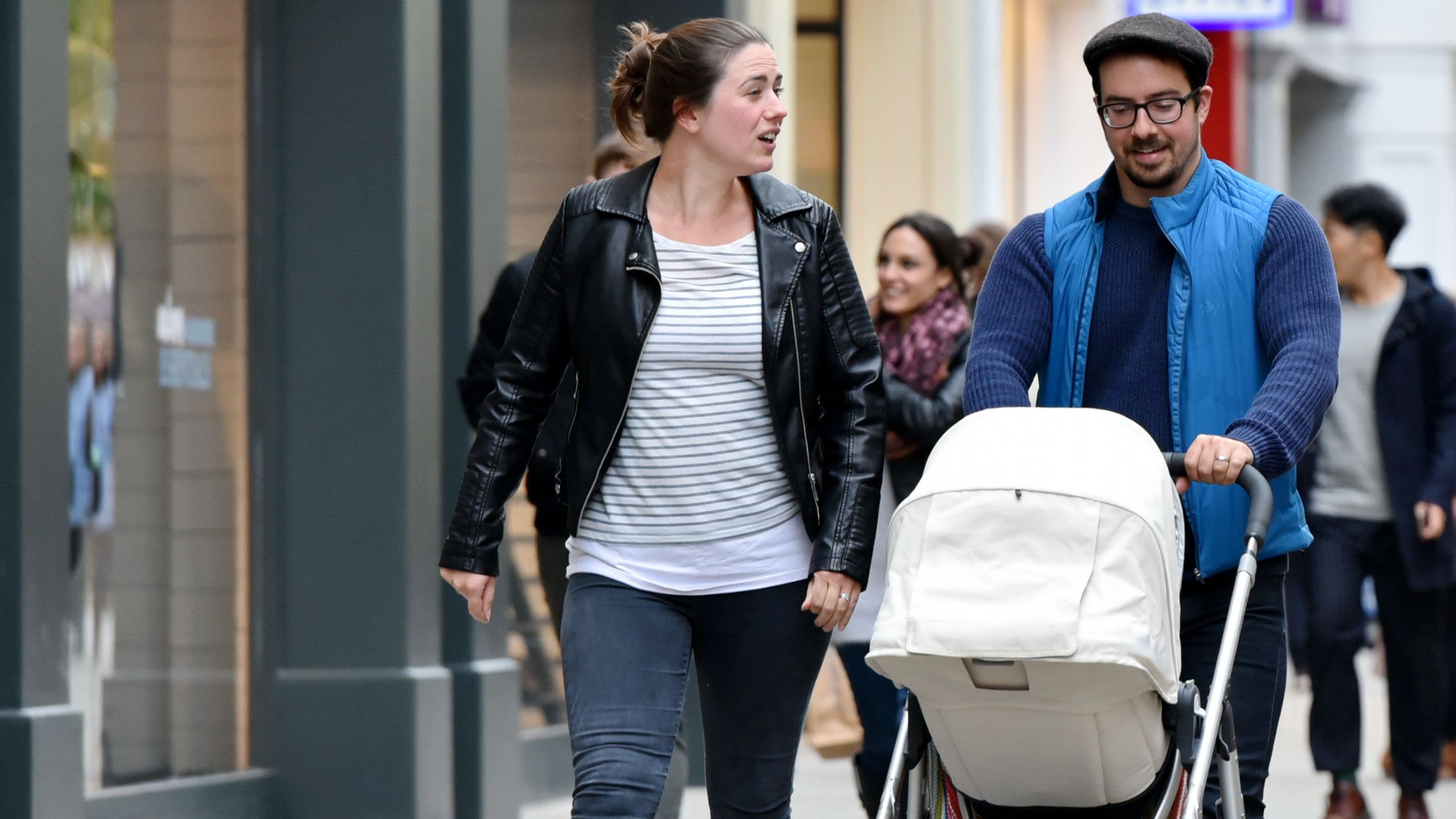 Adult couple walking along street pushing buggy