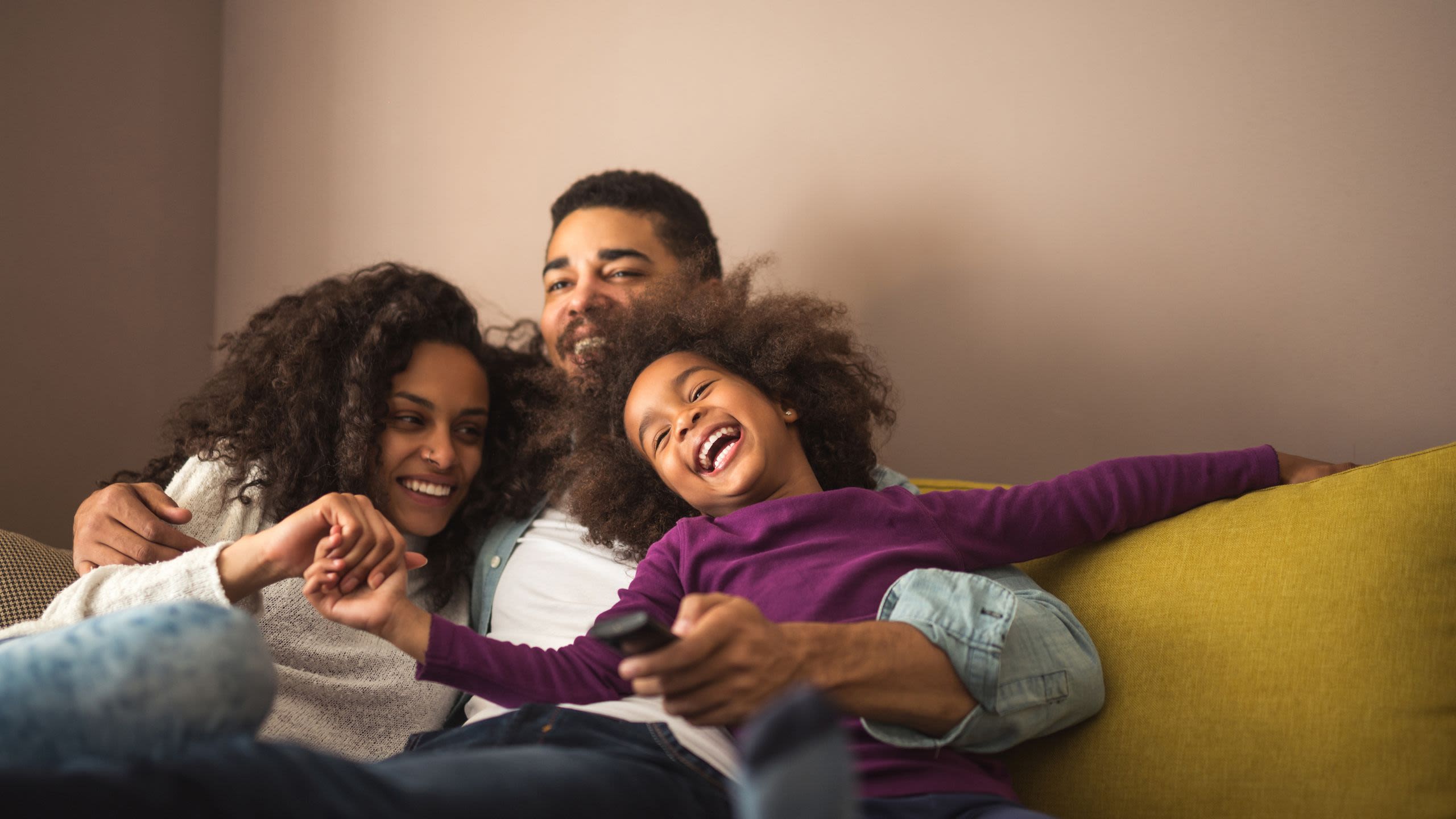 Parents and daughter on sofa laughing and cuddling