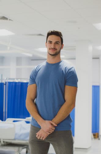 A young man stands confidently in a crisp, clean hospital environment