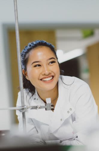 A young woman, wearing a lab coat, smiles as she conducts a science experiment
