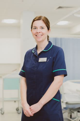 A woman, wearing a nursing uniform stands in a hospital environment