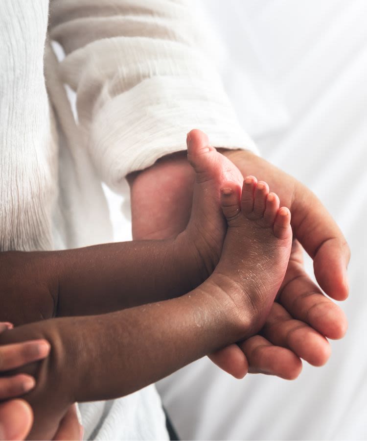 A adult cradles a baby's feet in the palm of their hand
