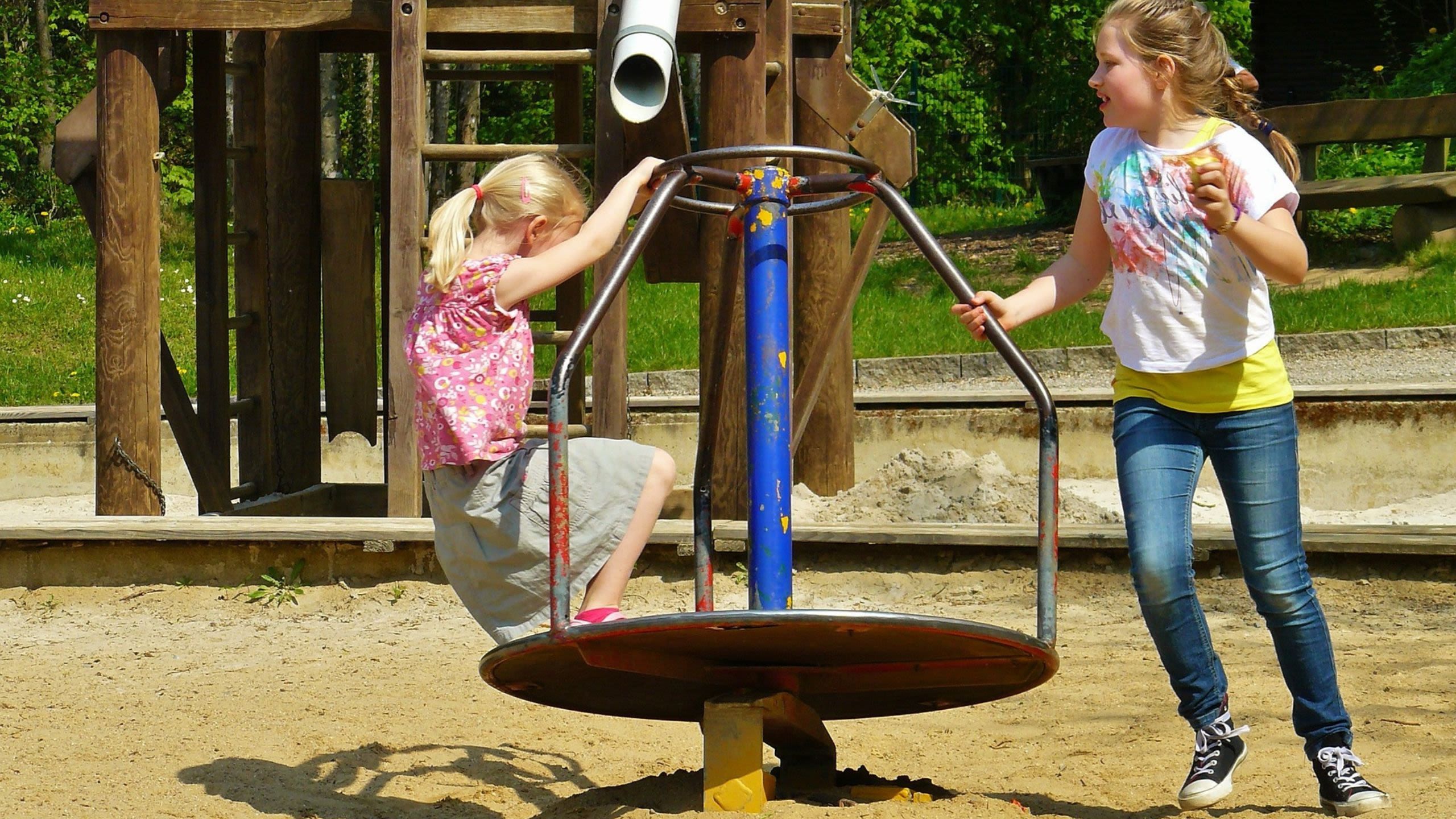 Two girls playing in small roundabout in playground