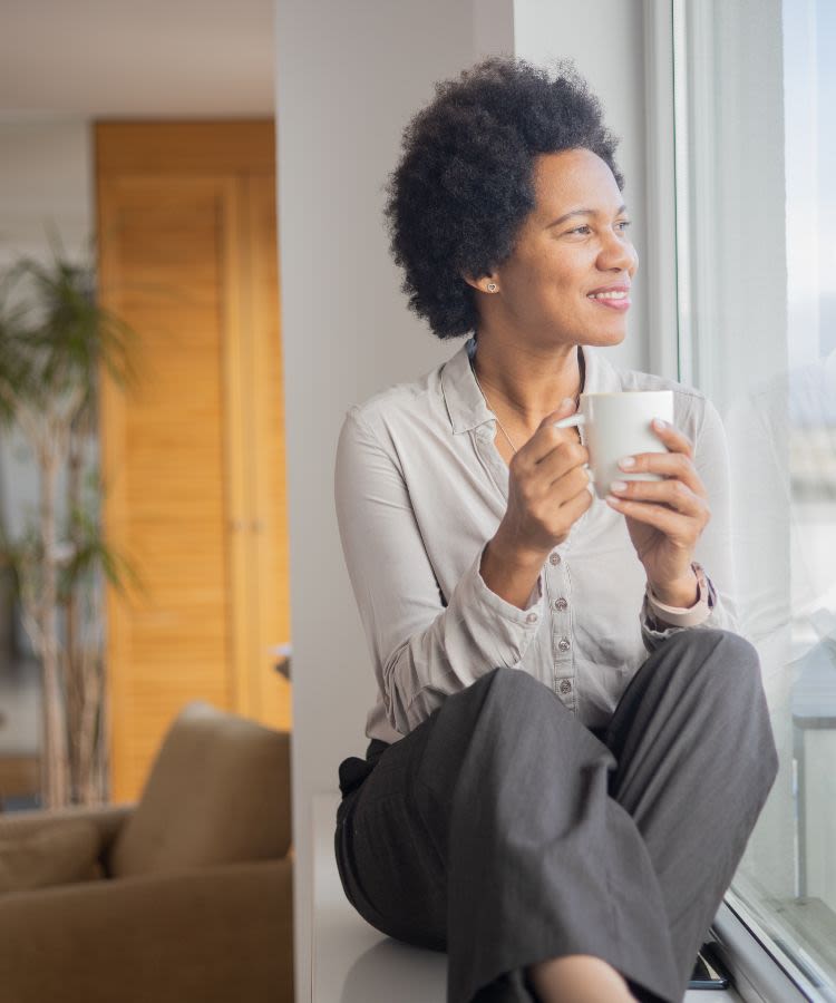 Woman sitting on windowsill looking out of window holding a mug