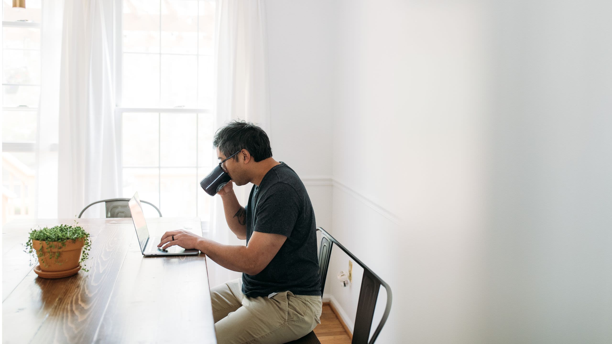 Man sipping coffee whilst looking at laptop