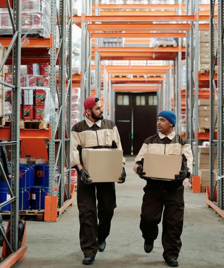 Two men carrying boxes walking in a warehouse