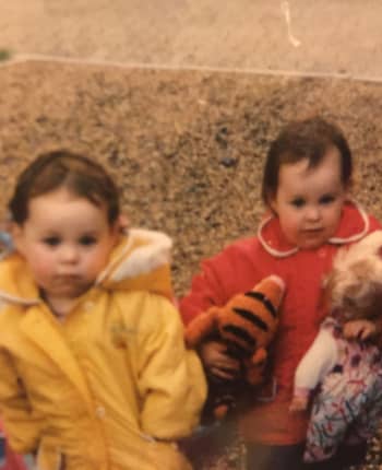 Two toddlers in raincoats. The image is grainy and clearly old.